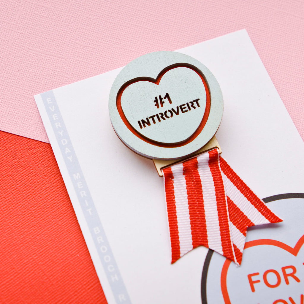 Candy & Kitsch candy heart merit brooch saying '#1 Introvert' that's made in Australia sits in a colourful background.