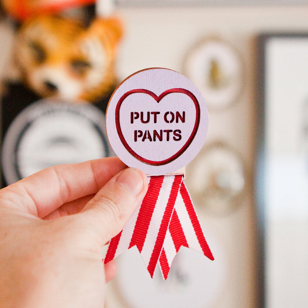 Candy & Kitsch motivational merit badge brooch saying 'put on pants' sits in a kitsch interior design aesthetic